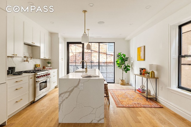 kitchen featuring light stone counters, decorative light fixtures, white cabinetry, an island with sink, and luxury stove