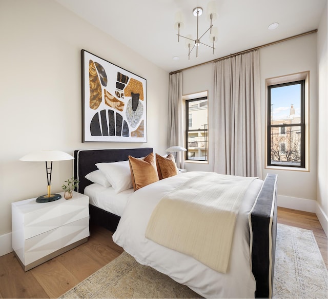 bedroom with light wood-style floors, multiple windows, baseboards, and an inviting chandelier