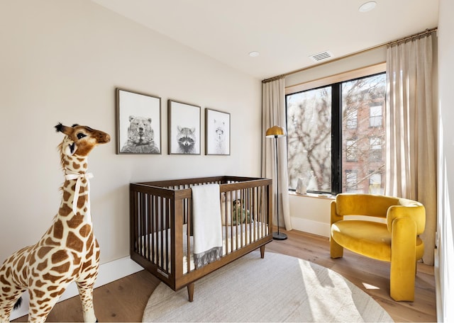 bedroom with a nursery area, baseboards, visible vents, and wood finished floors