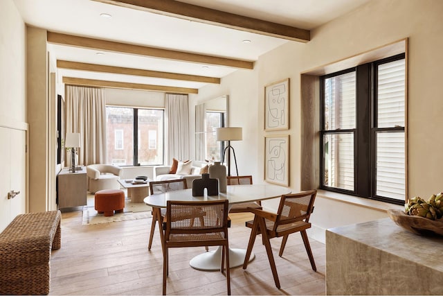 dining space featuring light wood finished floors and beamed ceiling