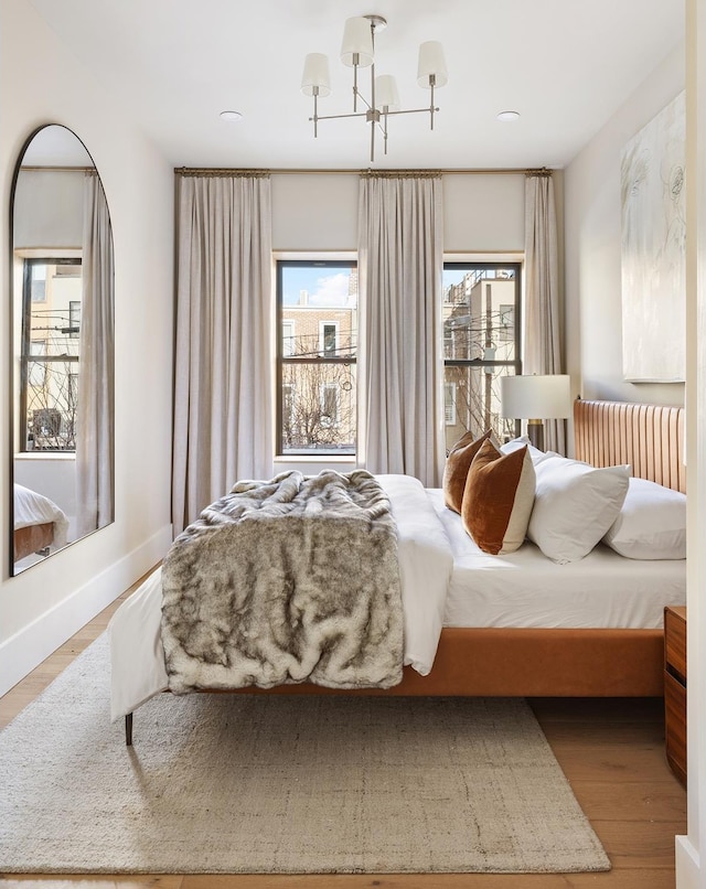 bedroom with radiator heating unit, baseboards, a chandelier, and wood finished floors