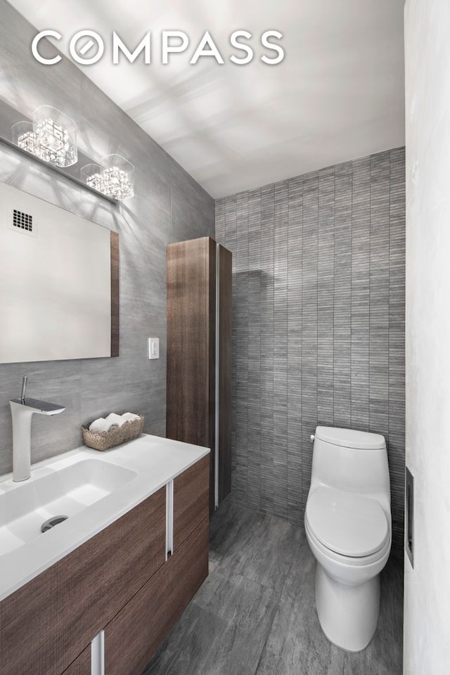 half bath featuring visible vents, toilet, vanity, and tile walls