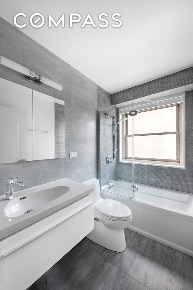 full bathroom featuring toilet, wood finished floors, vanity, tile walls, and washtub / shower combination