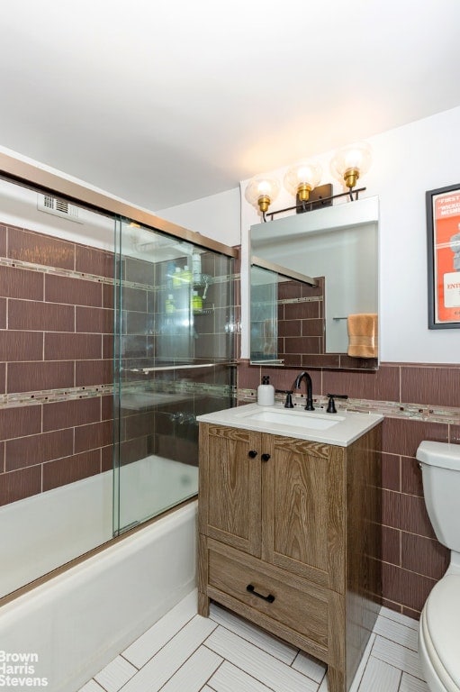 full bathroom with toilet, vanity, tile patterned flooring, tile walls, and shower / bath combination with glass door