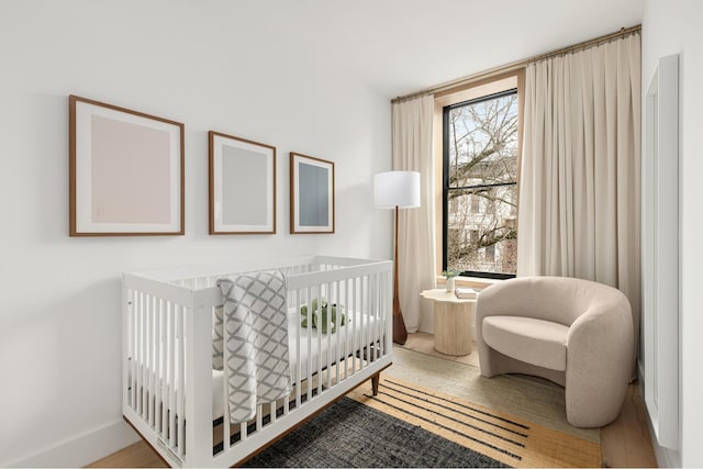 bedroom with a crib, wood finished floors, and baseboards