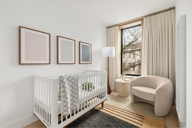 bedroom featuring a crib, wood finished floors, and baseboards