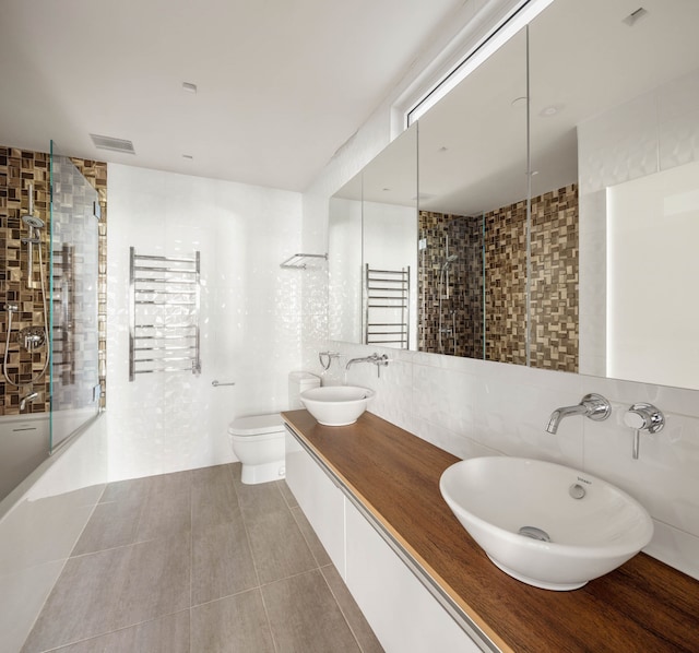 bathroom with tiled shower, tile walls, visible vents, and a sink