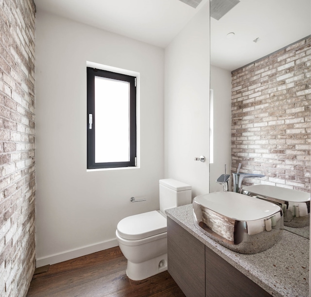 bathroom featuring toilet, a sink, brick wall, wood finished floors, and baseboards