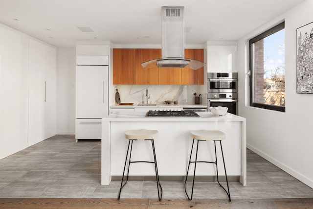 kitchen with island exhaust hood, light countertops, appliances with stainless steel finishes, white cabinetry, and modern cabinets