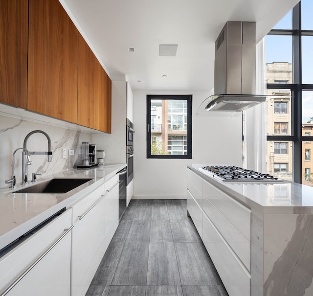 kitchen featuring a sink, white cabinets, appliances with stainless steel finishes, brown cabinetry, and island exhaust hood