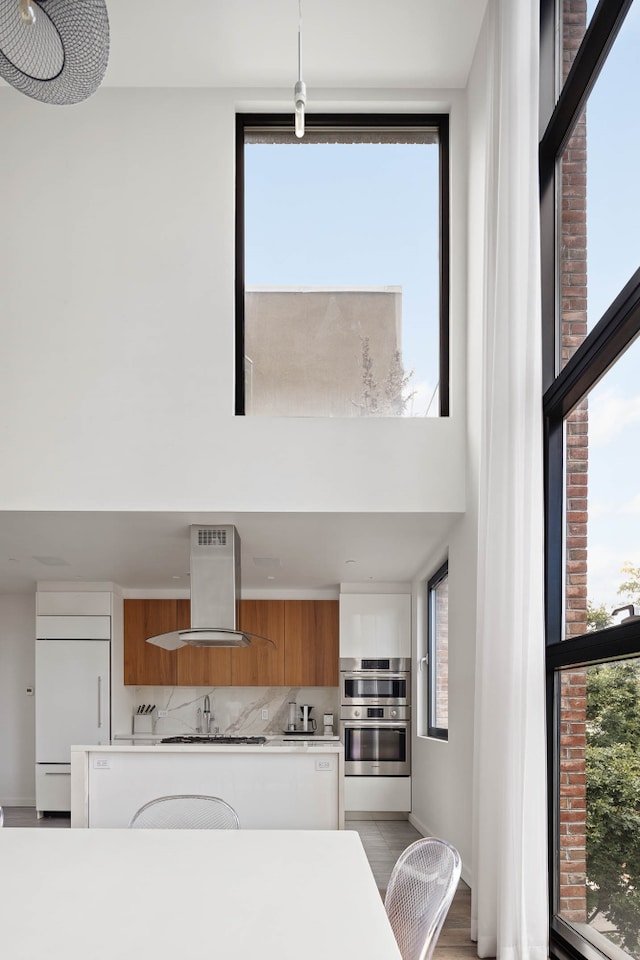 kitchen featuring brown cabinets, island exhaust hood, light countertops, white cabinets, and paneled refrigerator