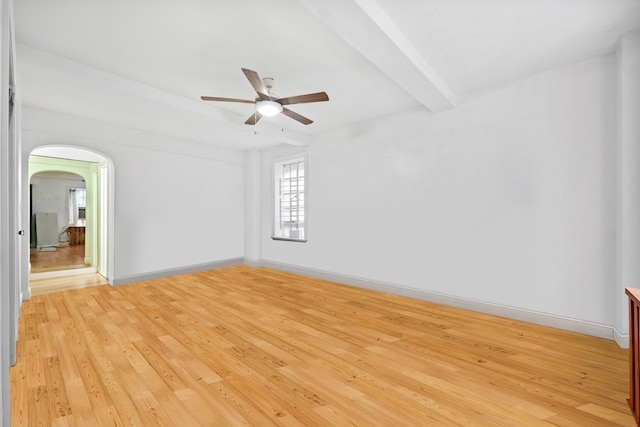 spare room with baseboards, arched walkways, a ceiling fan, light wood-type flooring, and beam ceiling