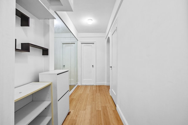 corridor featuring light wood-style flooring, baseboards, and arched walkways