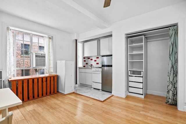 kitchen with light wood finished floors, white range with gas stovetop, beamed ceiling, freestanding refrigerator, and light countertops