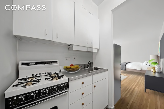 kitchen featuring white range with gas stovetop, wood finished floors, a sink, white cabinets, and light countertops