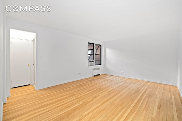 spare room with baseboards, radiator heating unit, and light wood-style floors