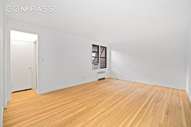 spare room with baseboards, radiator heating unit, and light wood-style floors