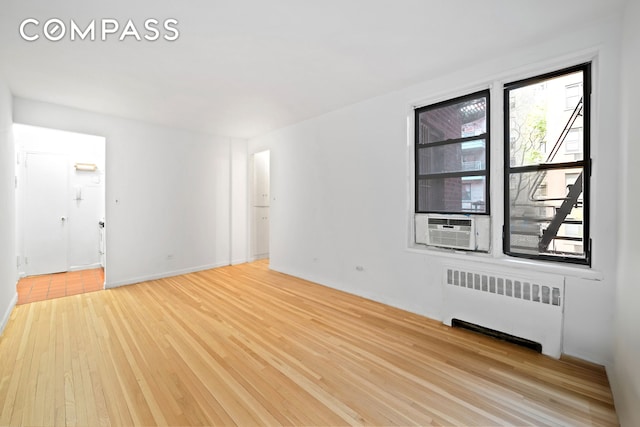unfurnished room featuring radiator heating unit, light wood-style flooring, and cooling unit
