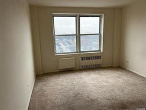 carpeted empty room featuring radiator heating unit