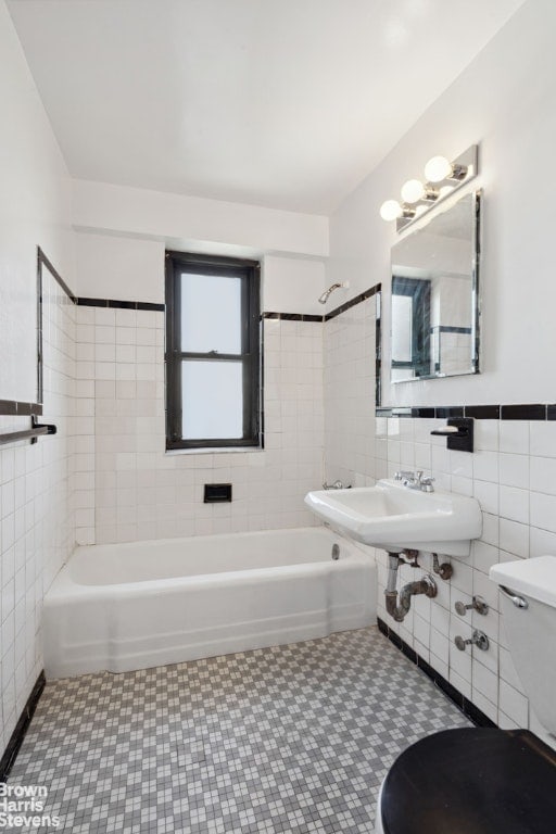 full bath featuring toilet, a sink, tile walls, and shower / bathtub combination