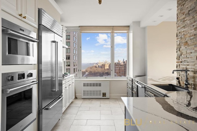 kitchen with white cabinetry, appliances with stainless steel finishes, sink, light stone counters, and radiator heating unit