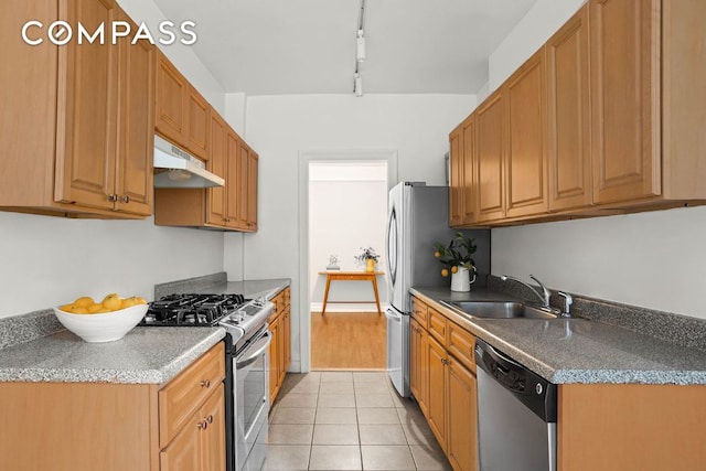 kitchen with light tile patterned floors, under cabinet range hood, stainless steel appliances, a sink, and brown cabinets