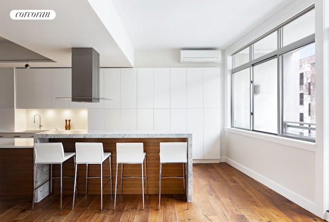 kitchen featuring light countertops, visible vents, a wall mounted AC, modern cabinets, and wall chimney exhaust hood