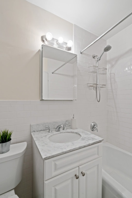 full bathroom featuring toilet, tile walls, tiled shower / bath, and vanity