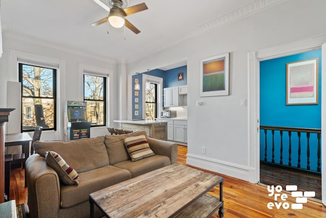 living room with light wood-type flooring, baseboards, ceiling fan, and crown molding