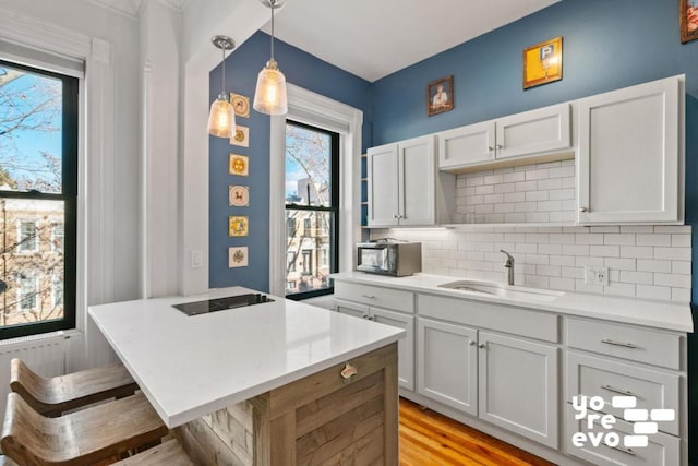 kitchen featuring a sink, white cabinets, light countertops, a kitchen bar, and pendant lighting