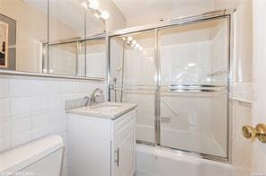 full bathroom featuring tile walls, shower / bath combination with glass door, vanity, and toilet