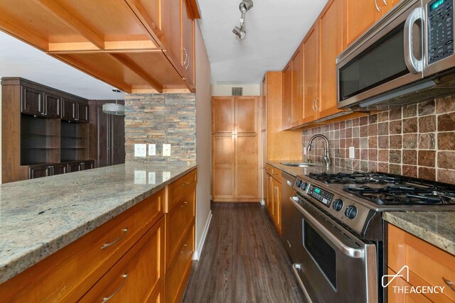 kitchen featuring stainless steel appliances, dark wood-type flooring, track lighting, light stone countertops, and sink