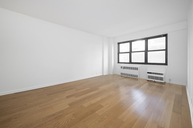 empty room with a wall mounted air conditioner, light wood-type flooring, baseboards, and radiator