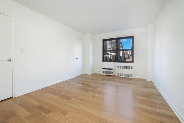 unfurnished room featuring an AC wall unit, radiator, electric panel, and light wood-type flooring