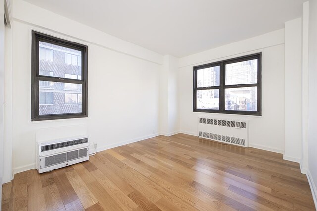 240 E 76th St Unit 7-M, New York City, NY 10021 - empty room with radiator heating unit, light wood-style floors, baseboards, and a wall mounted AC