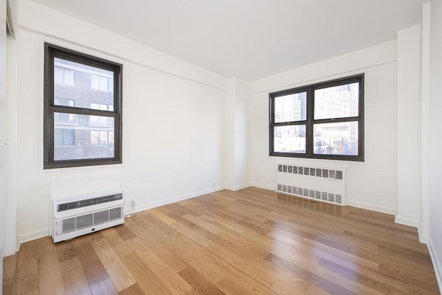 unfurnished room featuring a wall mounted AC, a wealth of natural light, radiator heating unit, and hardwood / wood-style flooring