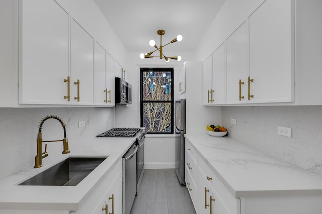 kitchen with a notable chandelier, a sink, backsplash, stainless steel appliances, and white cabinets