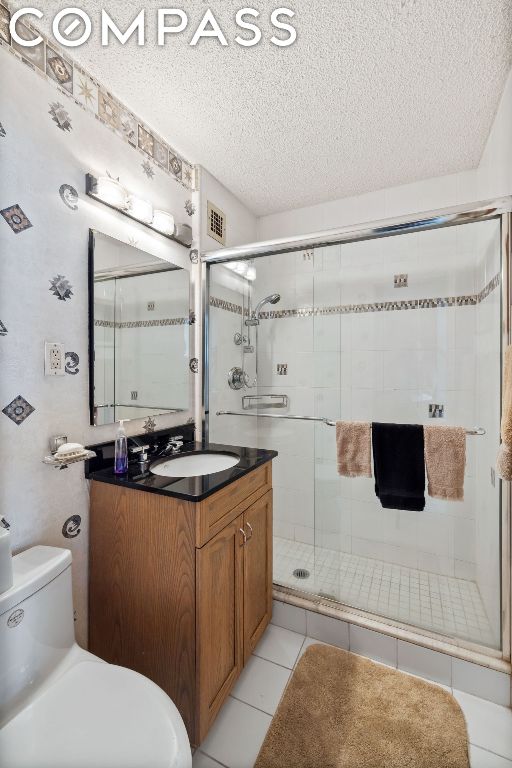 bathroom featuring a textured ceiling, tile patterned flooring, vanity, toilet, and walk in shower