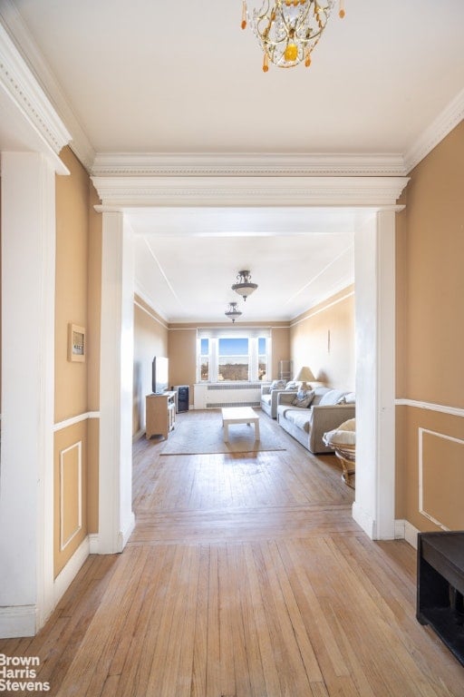 living area with a chandelier, ornamental molding, light wood-style flooring, and baseboards