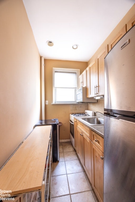 kitchen featuring dark countertops, backsplash, light tile patterned flooring, a sink, and white appliances