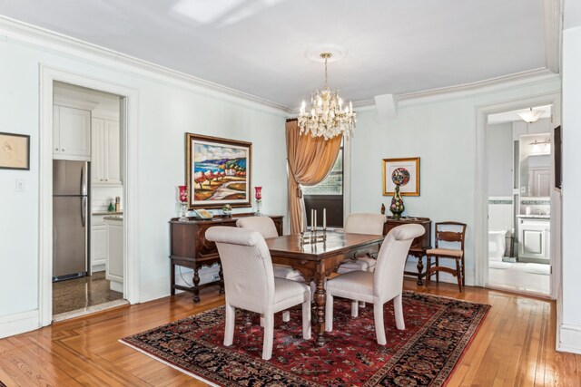 dining area with light wood-type flooring, baseboards, ornamental molding, and a notable chandelier