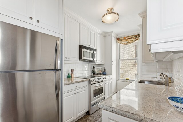 kitchen featuring stainless steel appliances, tasteful backsplash, white cabinetry, a sink, and light stone countertops