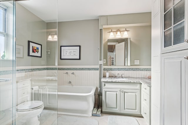 bathroom featuring tile walls, toilet, wainscoting, vanity, and a tub