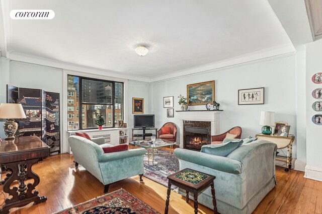 living room featuring wood-type flooring, crown molding, and a fireplace