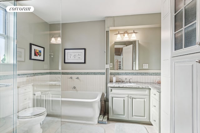 full bath featuring toilet, a wainscoted wall, vanity, tile walls, and a tub