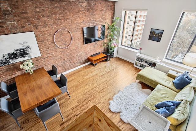 living room with plenty of natural light, wood finished floors, baseboards, and brick wall