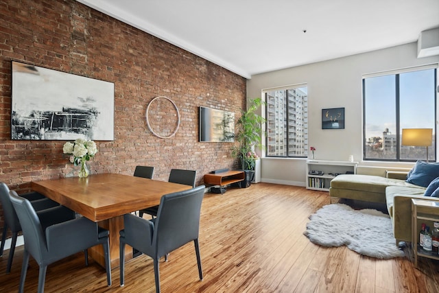 dining space featuring brick wall, baseboards, and wood-type flooring