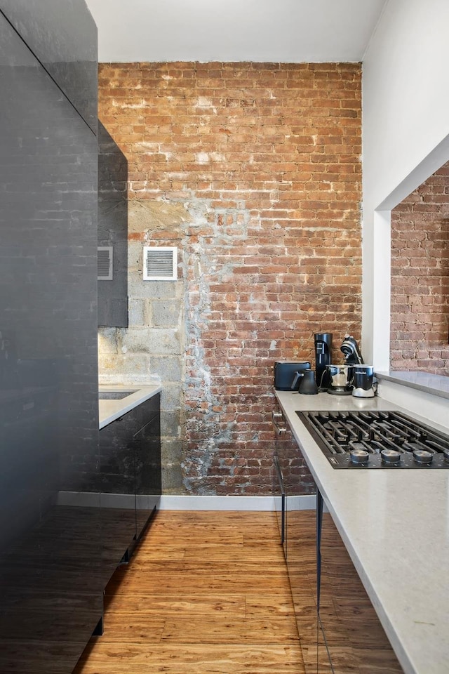 kitchen featuring visible vents, stovetop, light wood-style floors, brick wall, and light countertops