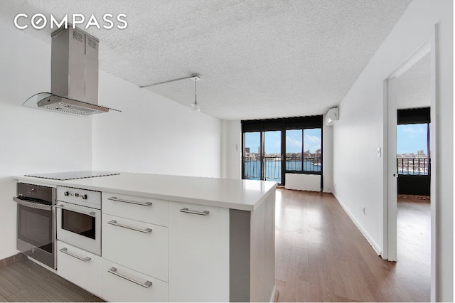 kitchen with island range hood, white oven, stainless steel oven, light countertops, and white cabinetry