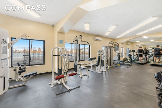 gym featuring a wealth of natural light, a wall mounted air conditioner, and a textured ceiling